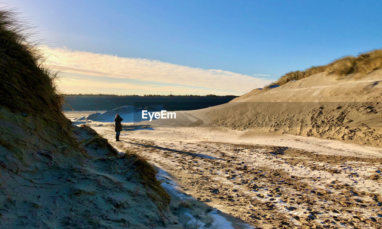 Early winter sun shines on a landscape with dunes between which someone is looking with binoculars