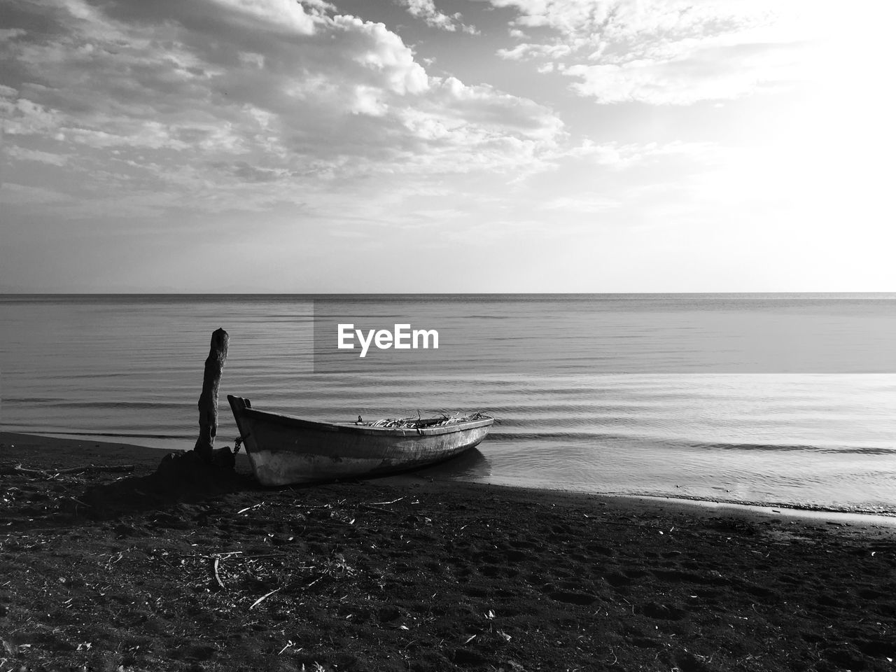 Boat moored on beach against cloudy sky