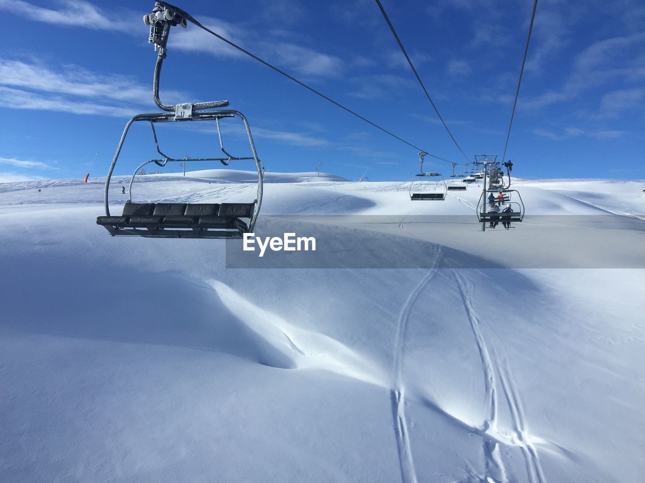 Low angle view of ski lift over snowy field against cloudy sky during sunny day