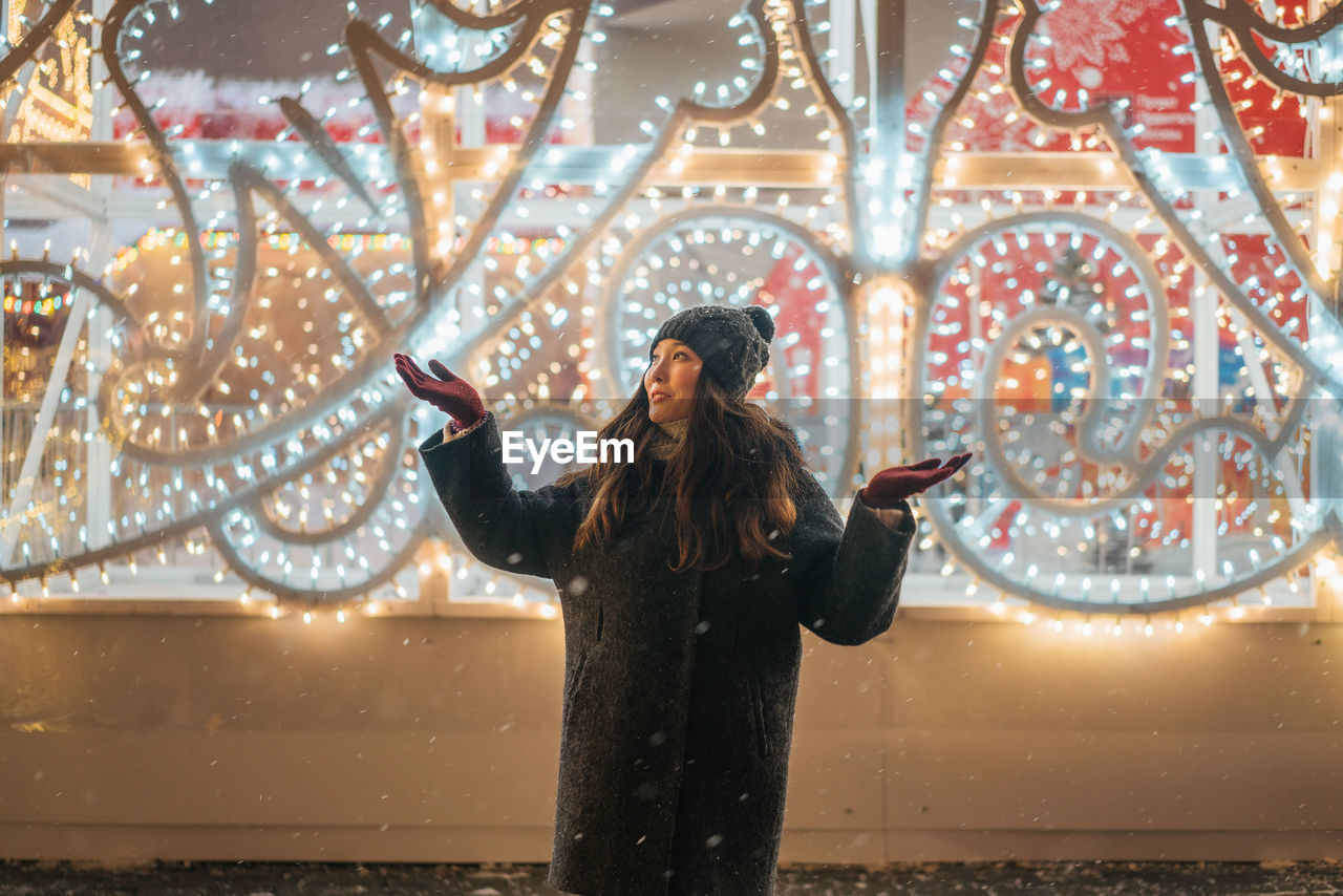 FULL LENGTH OF A YOUNG WOMAN AT ILLUMINATED CAROUSEL