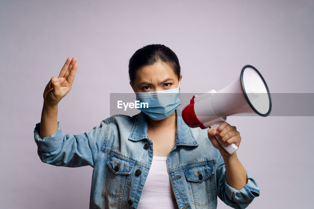 Close-up of young woman wearing flu mask holding megaphone against white background