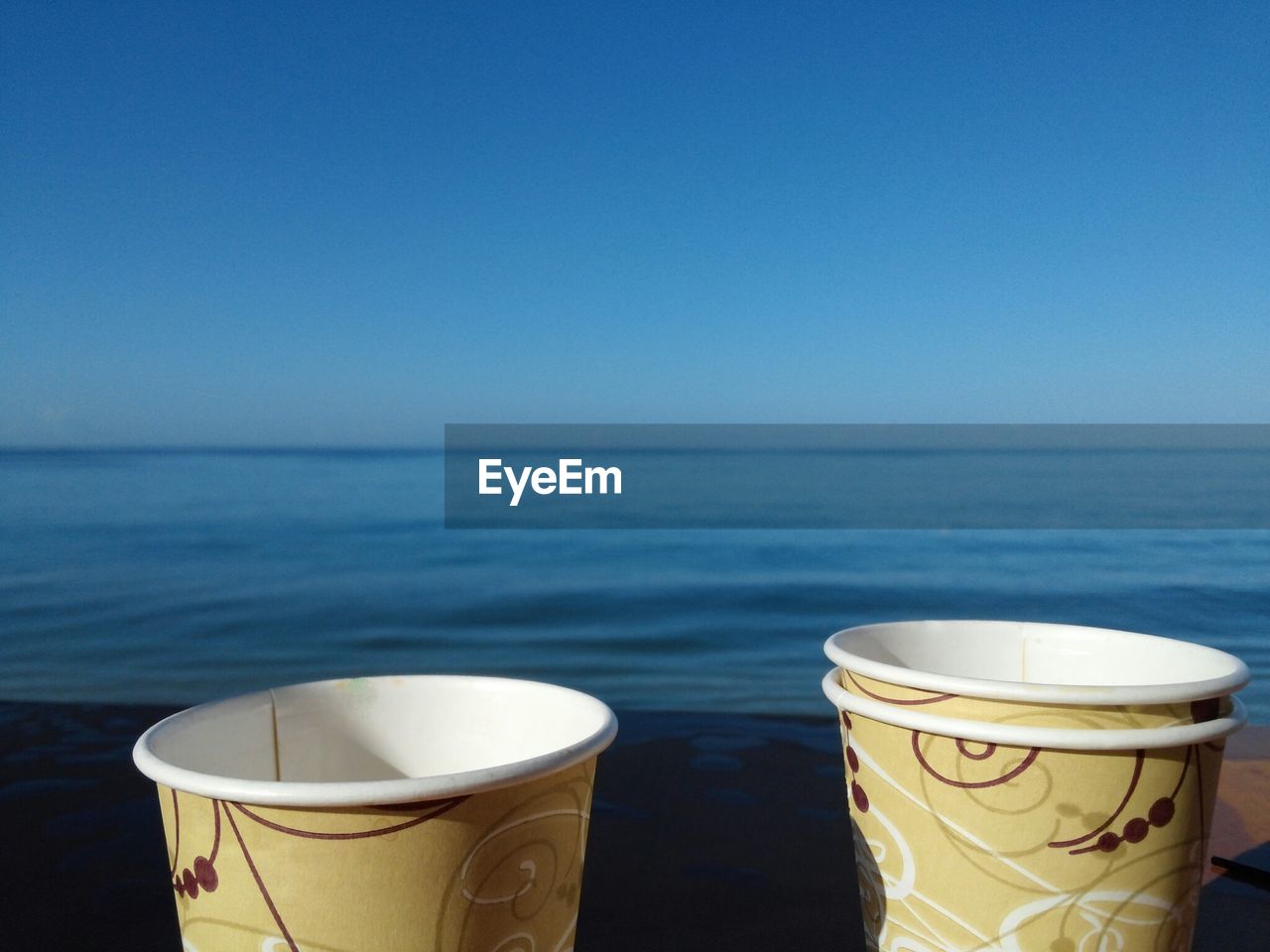 COFFEE CUP AND SEA AGAINST CLEAR SKY