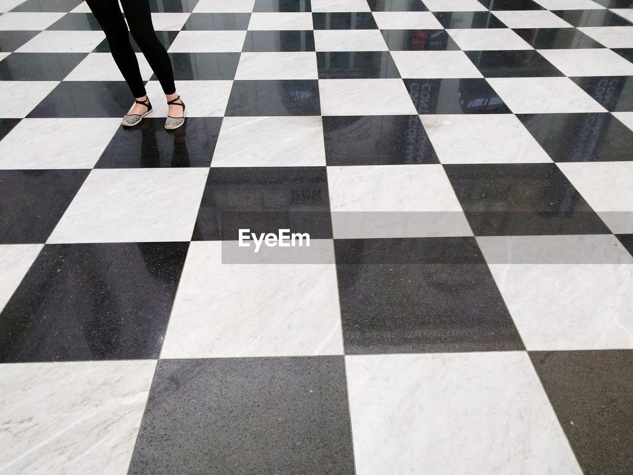 Low section of woman standing on checked pattern floor