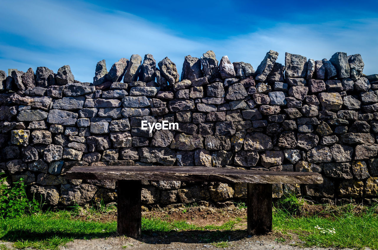 Empty bench against stone wall