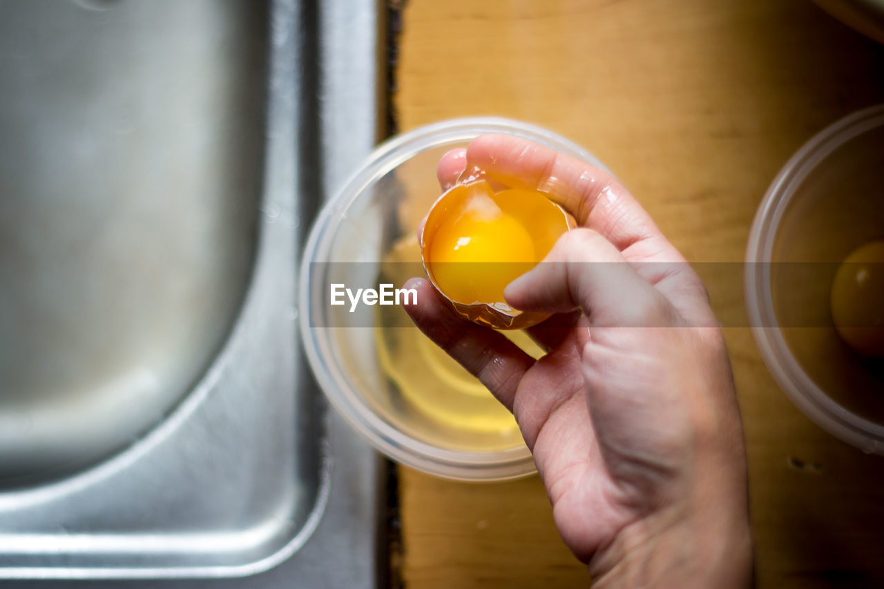 Cropped image of hand holding broken egg in kitchen