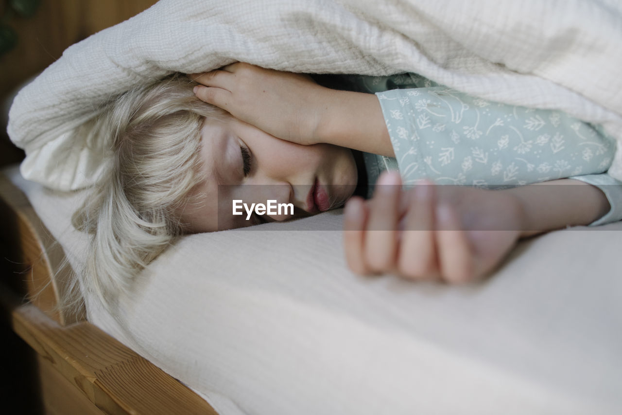 Girl sleeping under blanket on bed at home