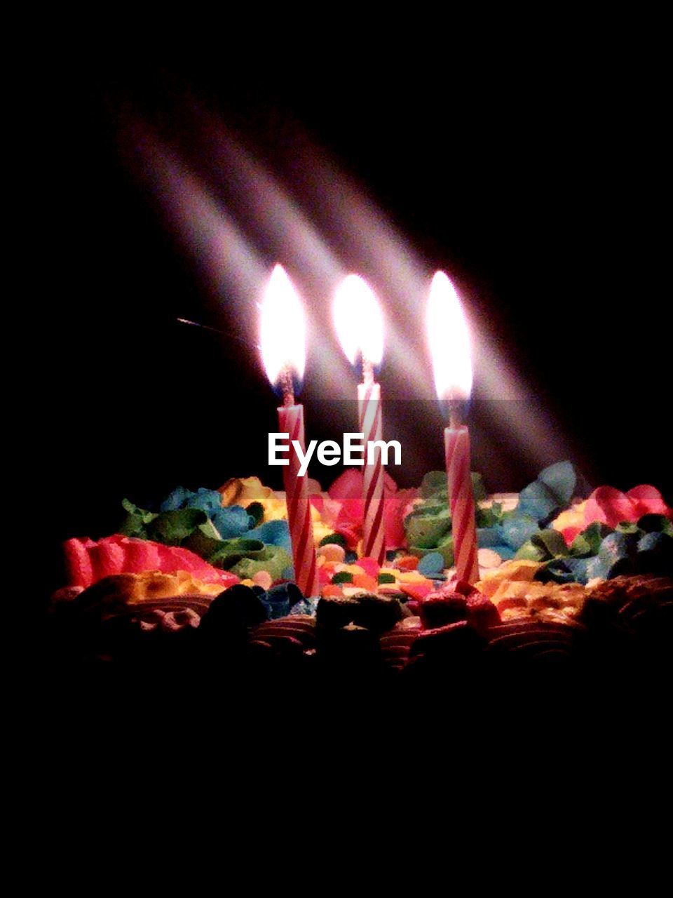 Close-up of burning birthday candles on cake in darkroom