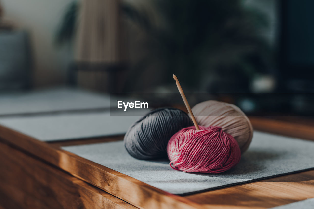 Balls of yarn with a wooden crochet hook on a wooden table, sunlight from the window, shallow focus.