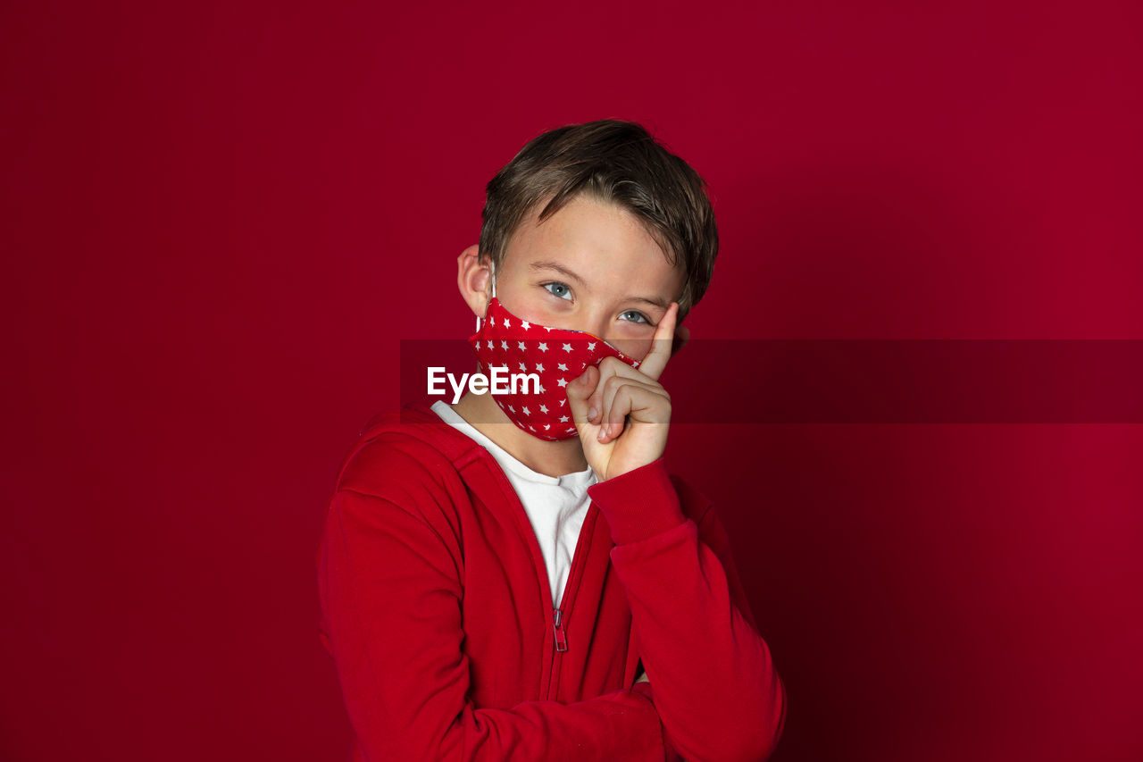 Cute boy wearing mask against red background