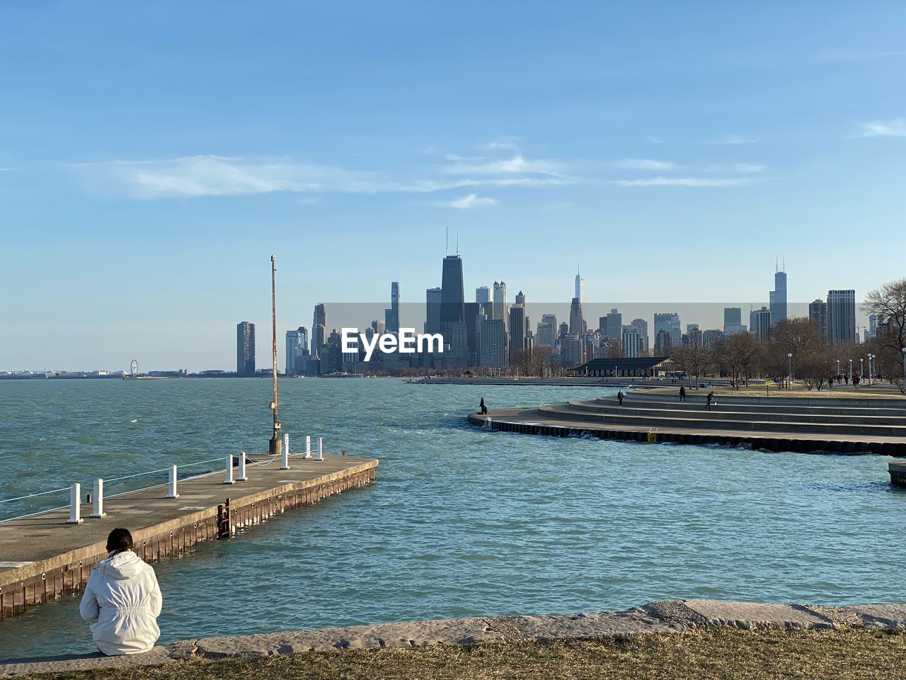 REAR VIEW OF PEOPLE LOOKING AT SEA BY CITY AGAINST SKY