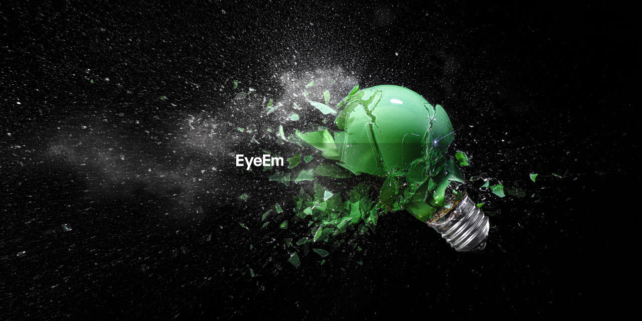 Green electric light bulb exploding on black.