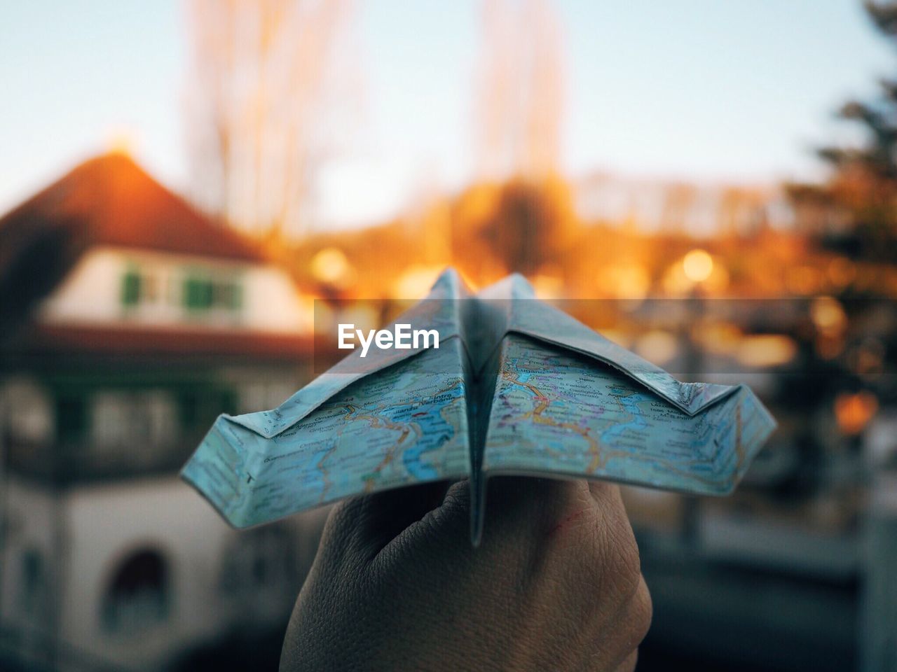 Cropped image of hand holding paper airplane made of map against houses