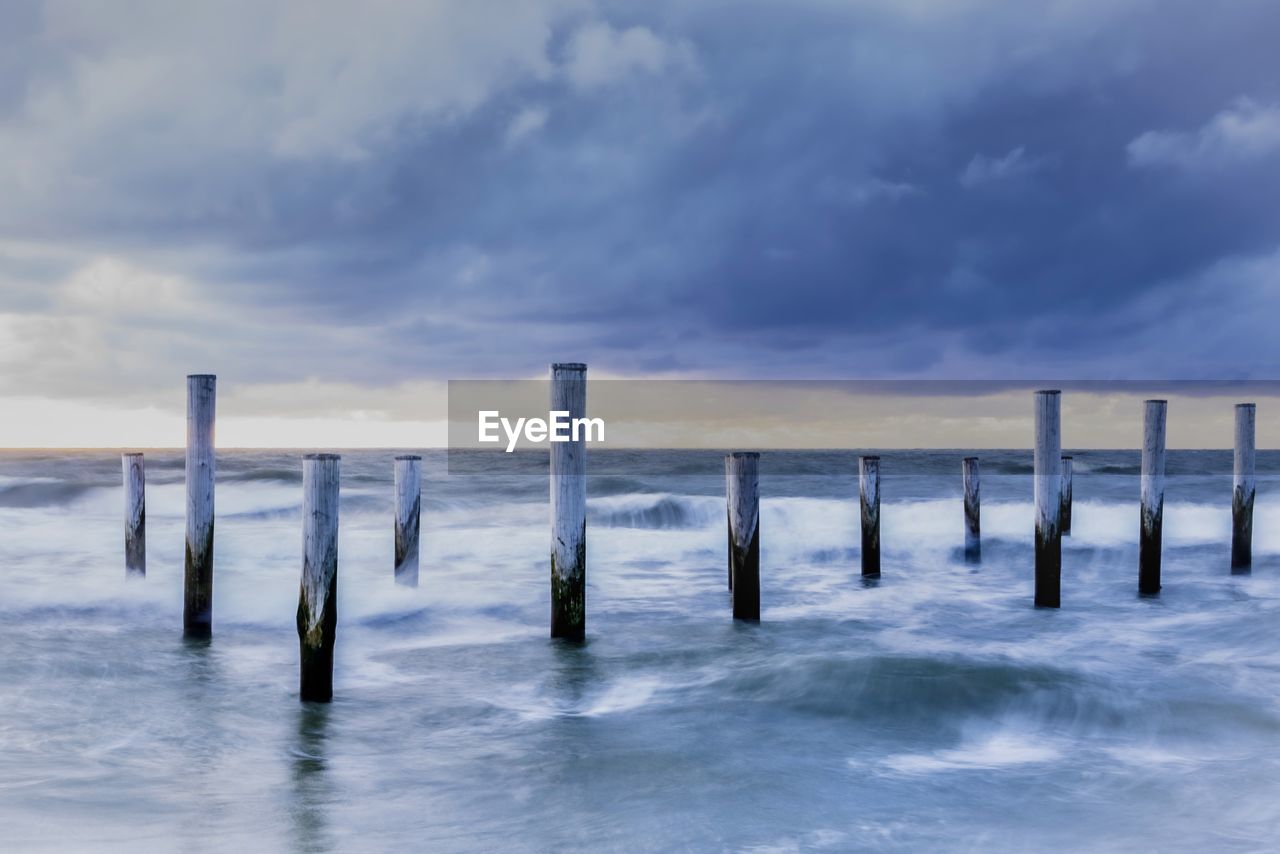 Wooden posts in sea against sky