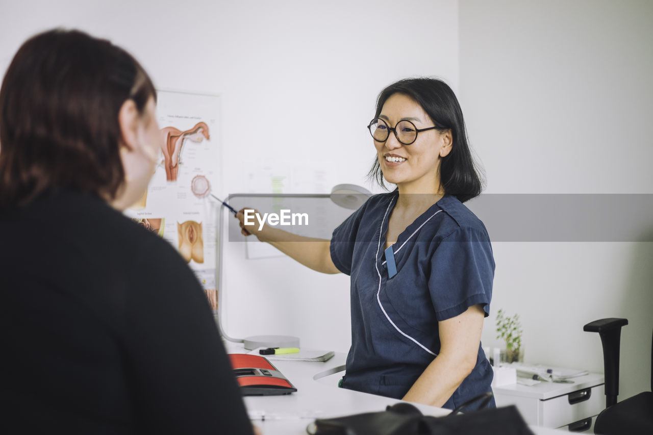 Happy mature doctor explaining organs to patient while pointing at chart in medical clinic