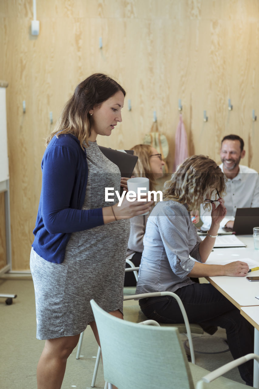 Pregnant businesswoman walking towards conference table in meeting