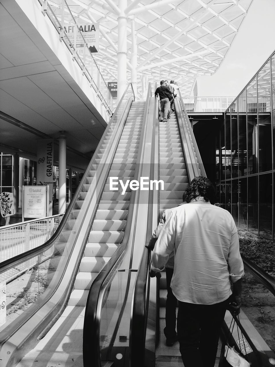 REAR VIEW OF MAN WALKING ON ESCALATOR