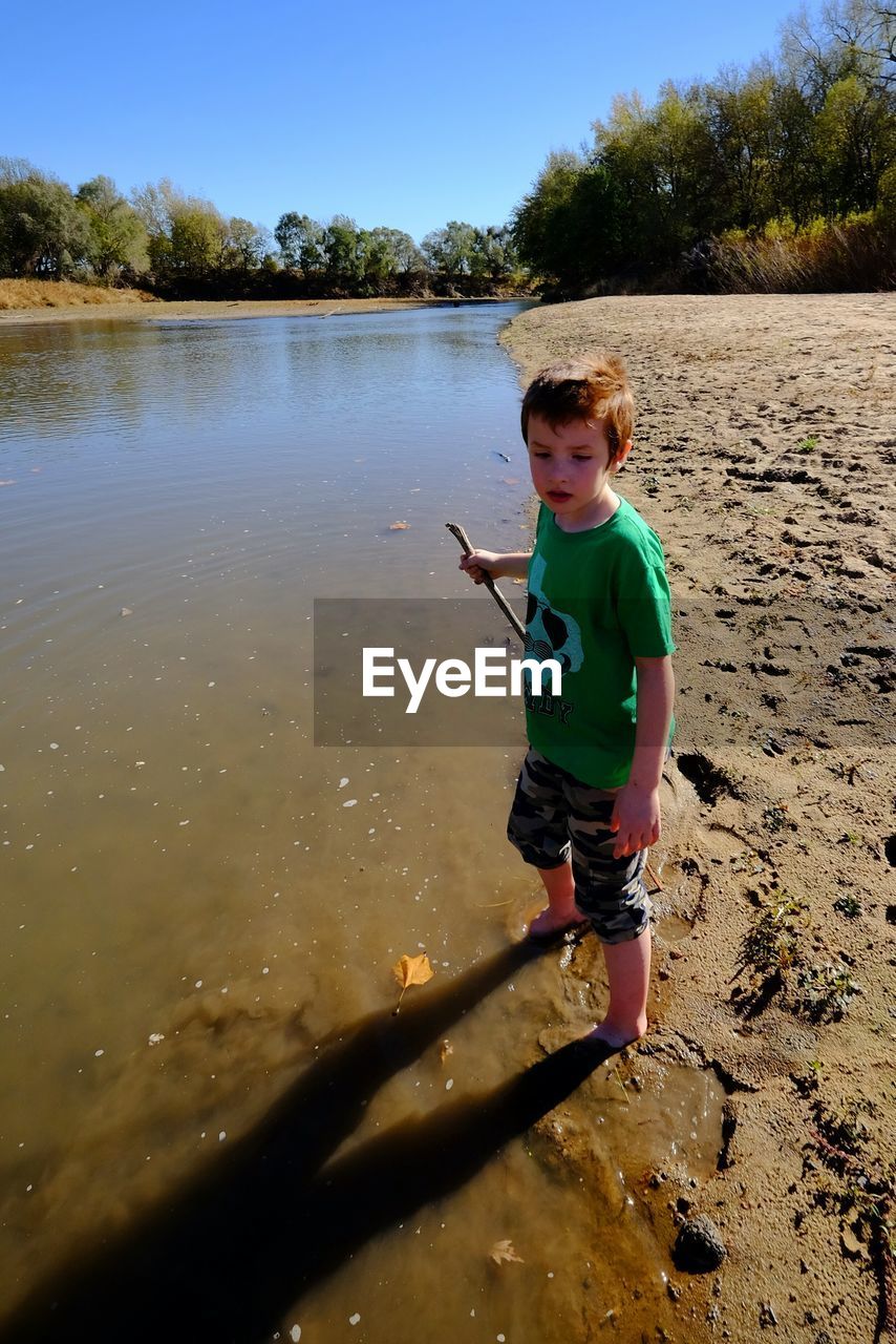 High angle view of boy holding stick while standing at little blue river