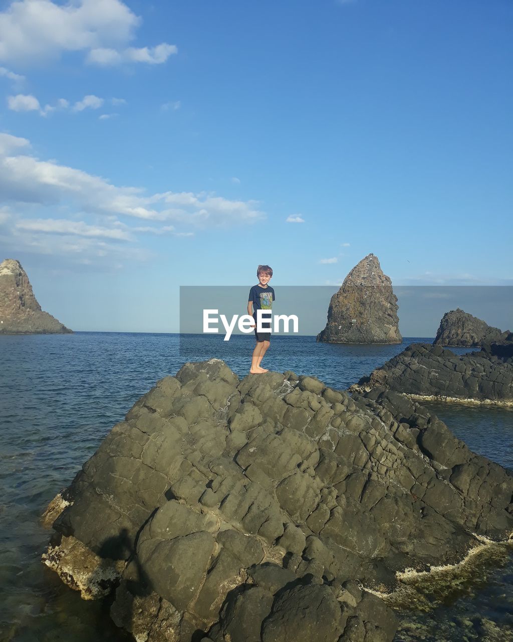 MAN STANDING ON ROCK AGAINST SEA