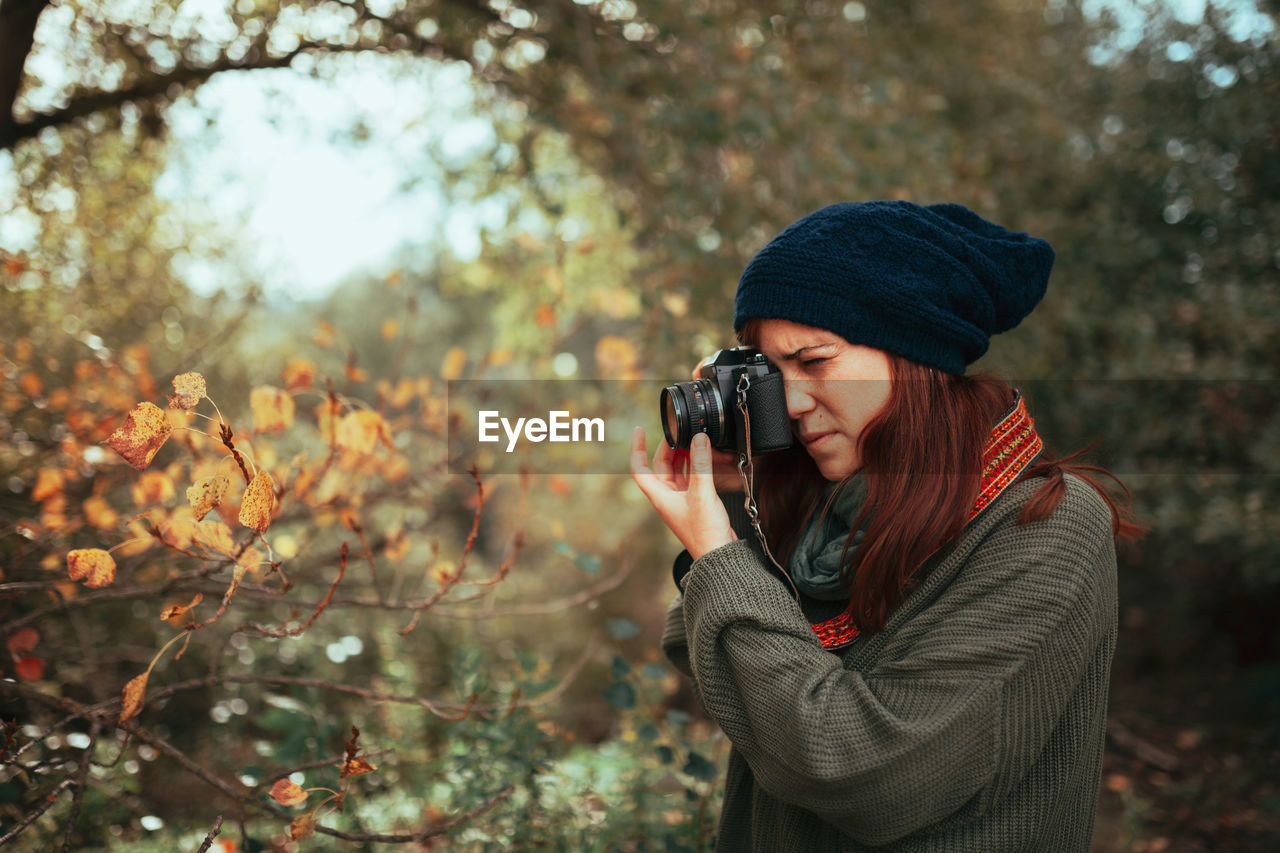 Young woman taking photos in the forest with an old analog camera