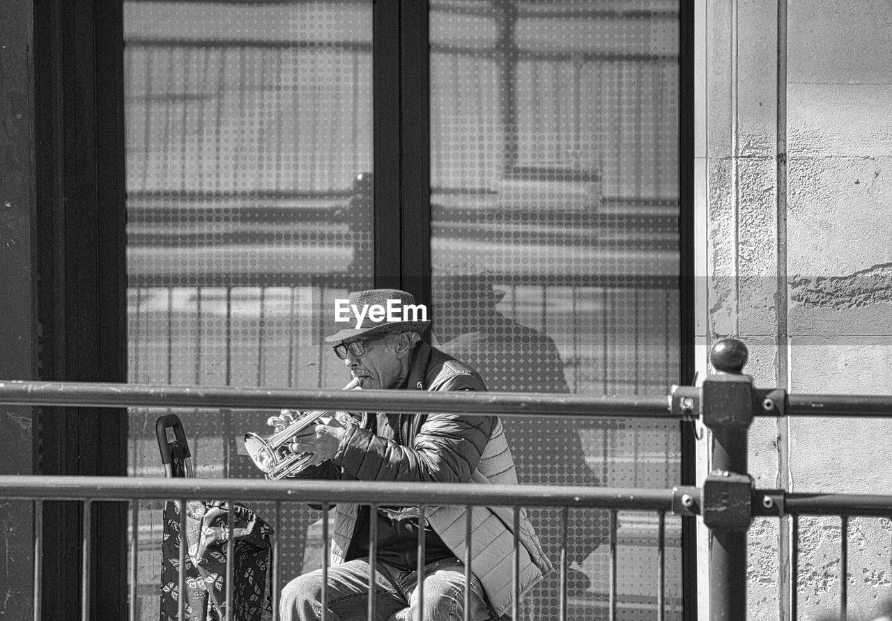 black and white, black, monochrome, monochrome photography, architecture, men, window, white, day, street, sitting, adult, lifestyles, person, clothing, built structure, one person, hat, outdoors, women, building exterior, leisure activity