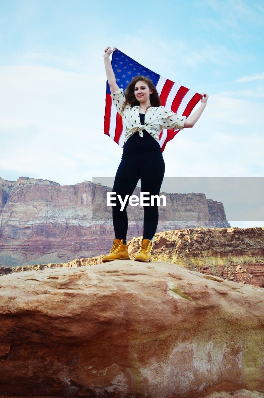 Low angle view of young woman holding american flag while standing in rocks at grand canyon