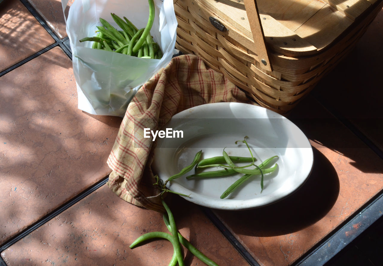 High angle view of green peas by wicker basket on table