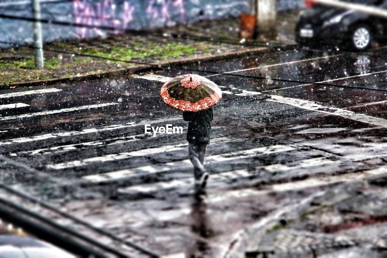 Person with umbrella crossing road during rainfall