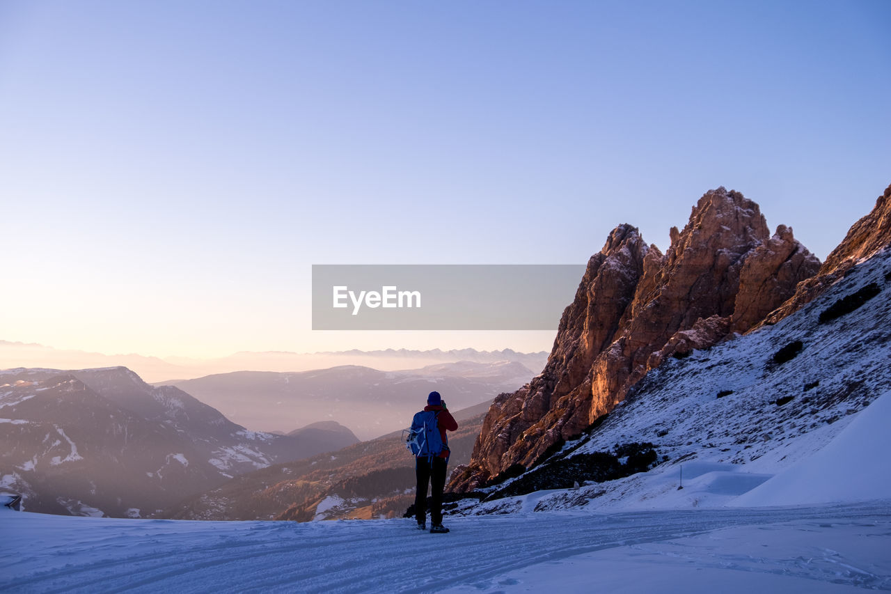 Rear view of man standing on snowcapped mountain against clear sky