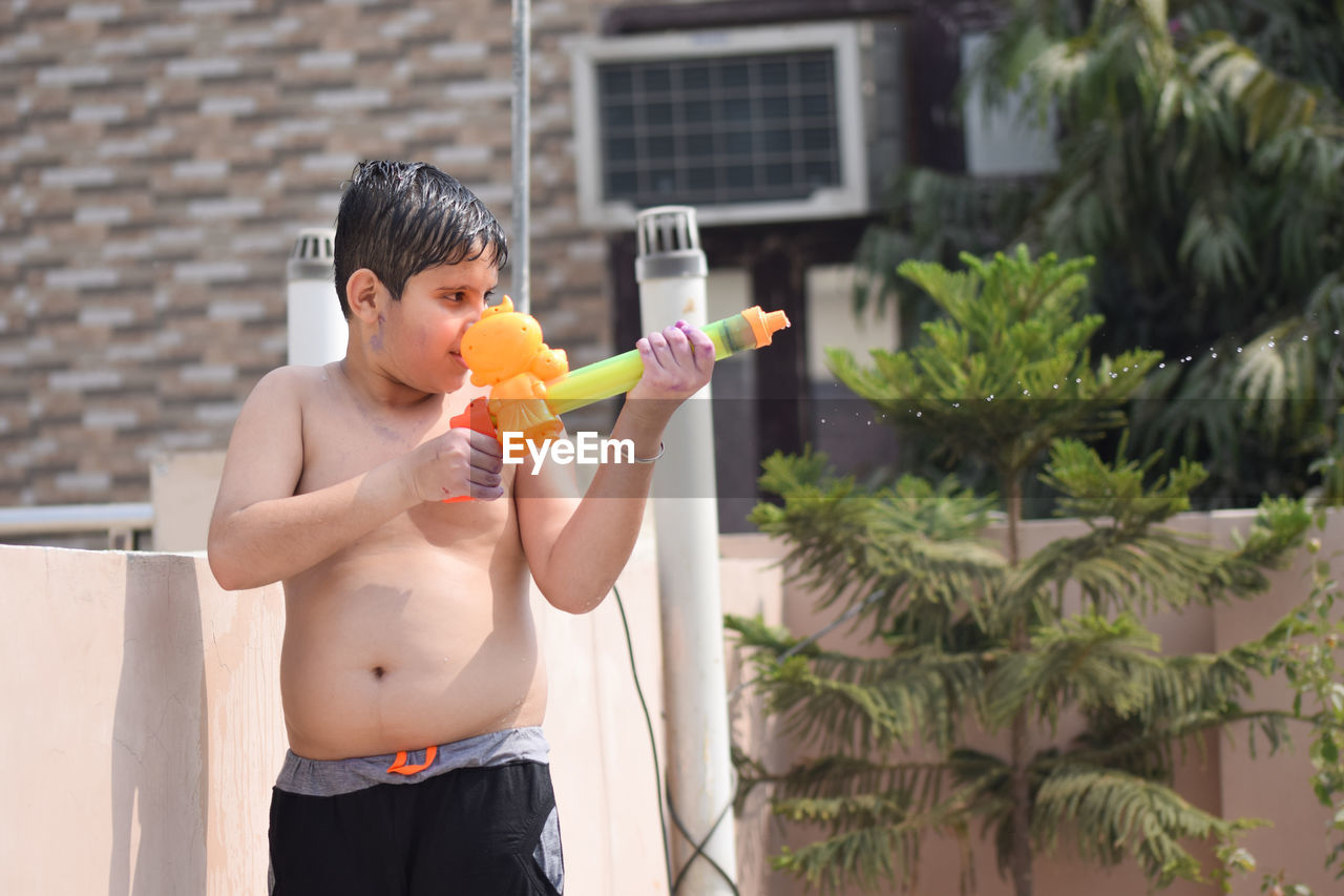 Shirtless boy playing with squirt gun during holi