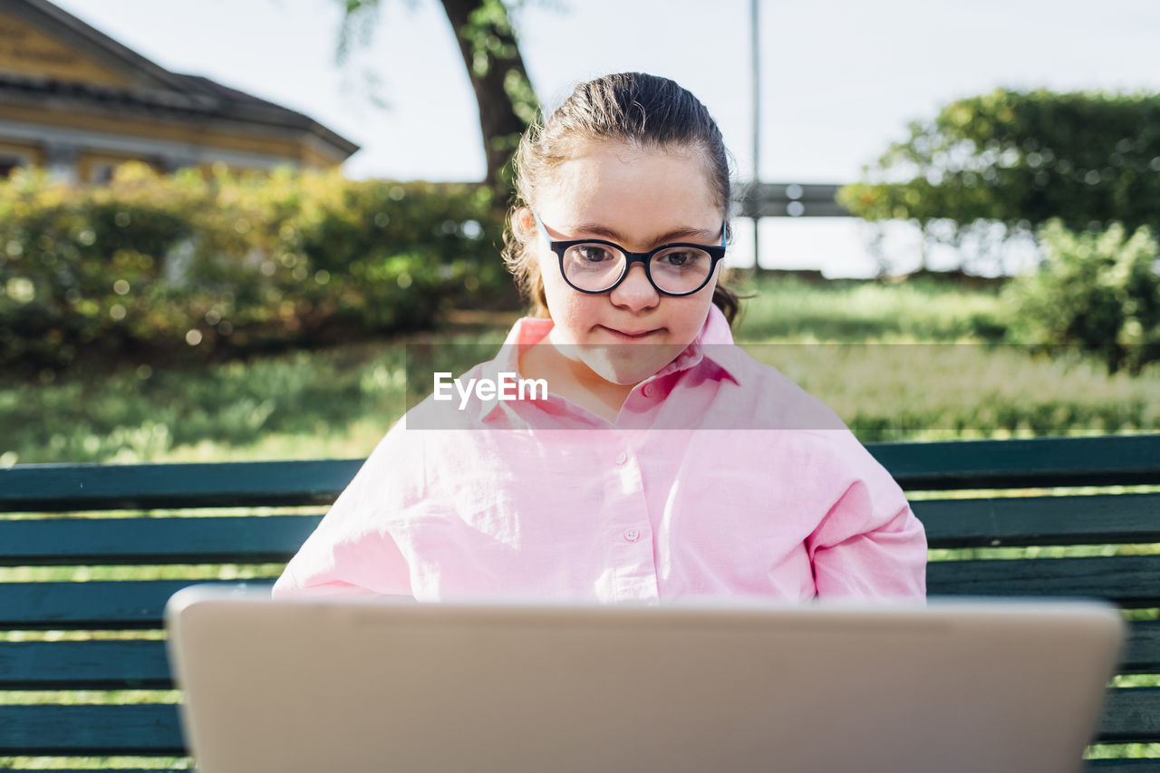 Teenage girl with down syndrome using laptop in park