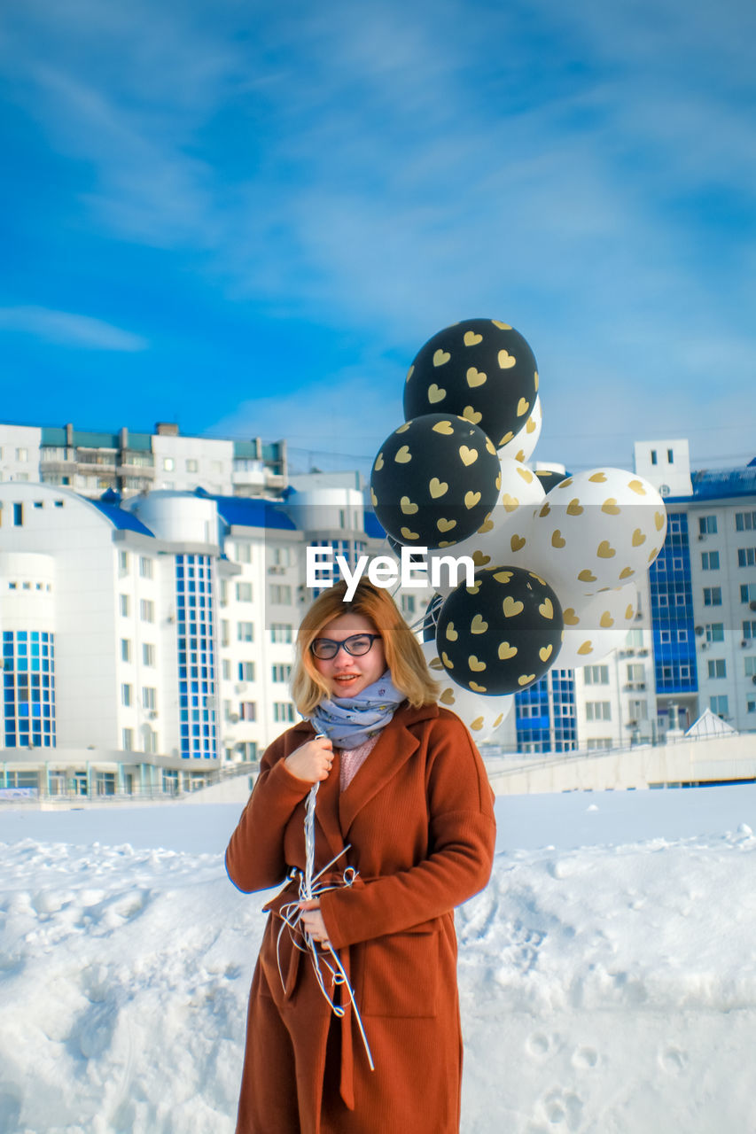 Portrait of woman with balloons standing on snow against sky