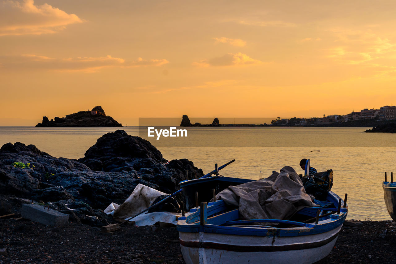 Fishing boat on pebble beach in lachea, homer's famous cyclops island in the odyssey, sicily, italy