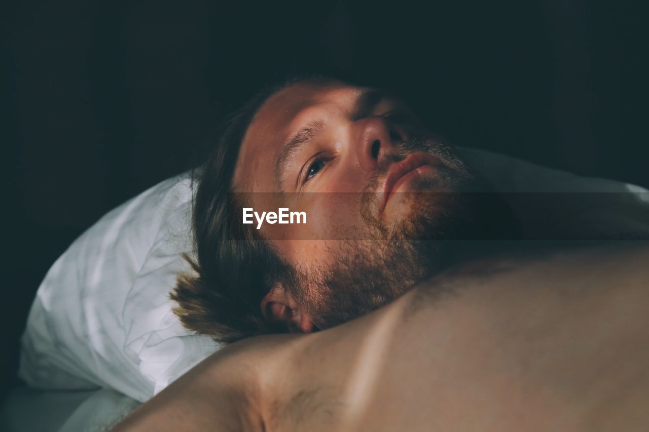 Close-up of thoughtful shirtless man looking away while lying down on bed