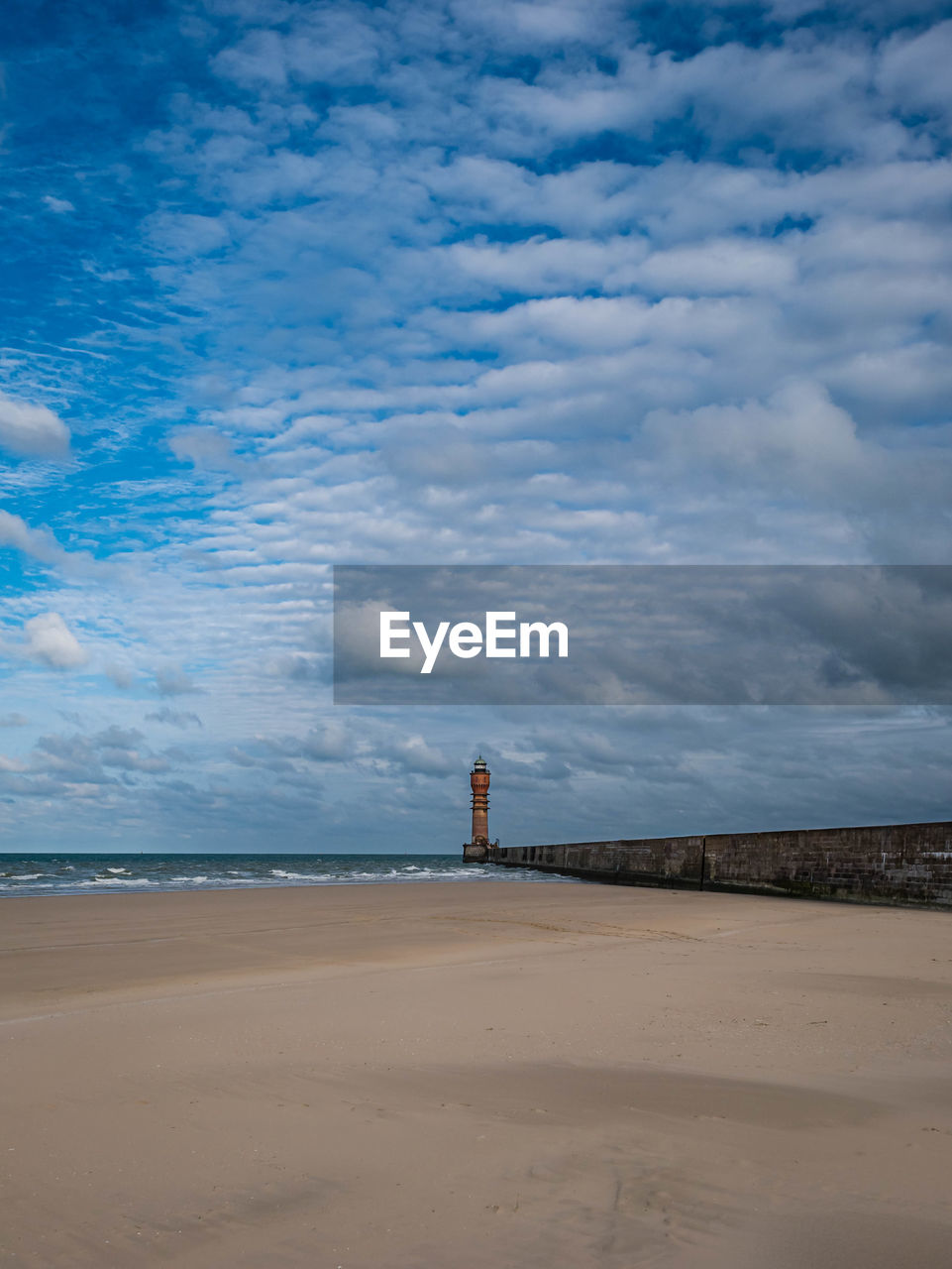 Lighthouse in the distance with pier at the beach leading towards it