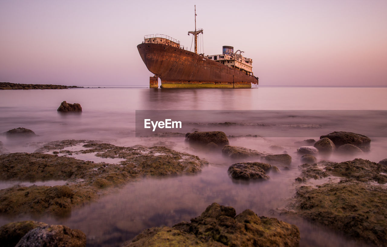 Abandoned ship on sea during sunset