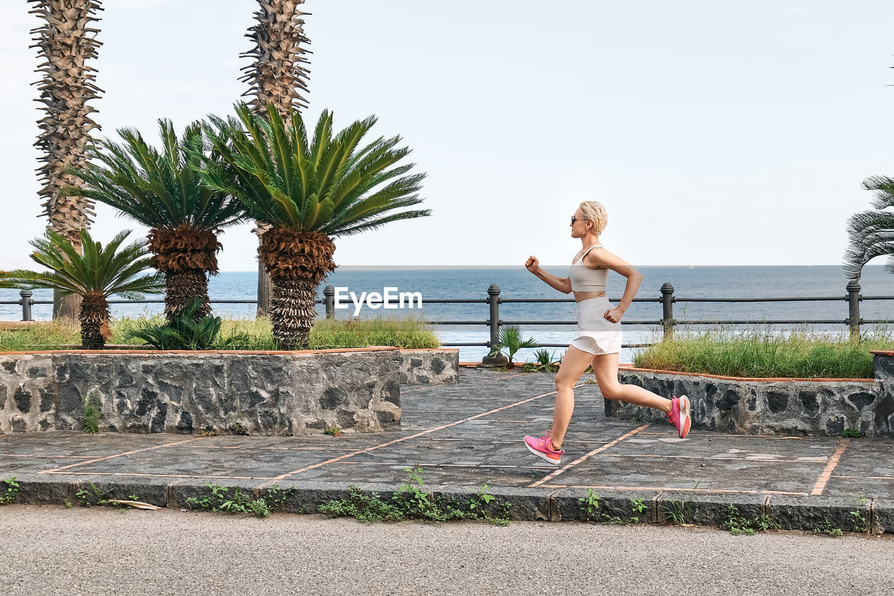 Young attractive sportive woman running on seaside promenade. workout outdoors by the sea.