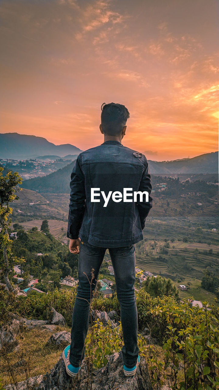 Rear view of man looking at mountains against sky during sunset