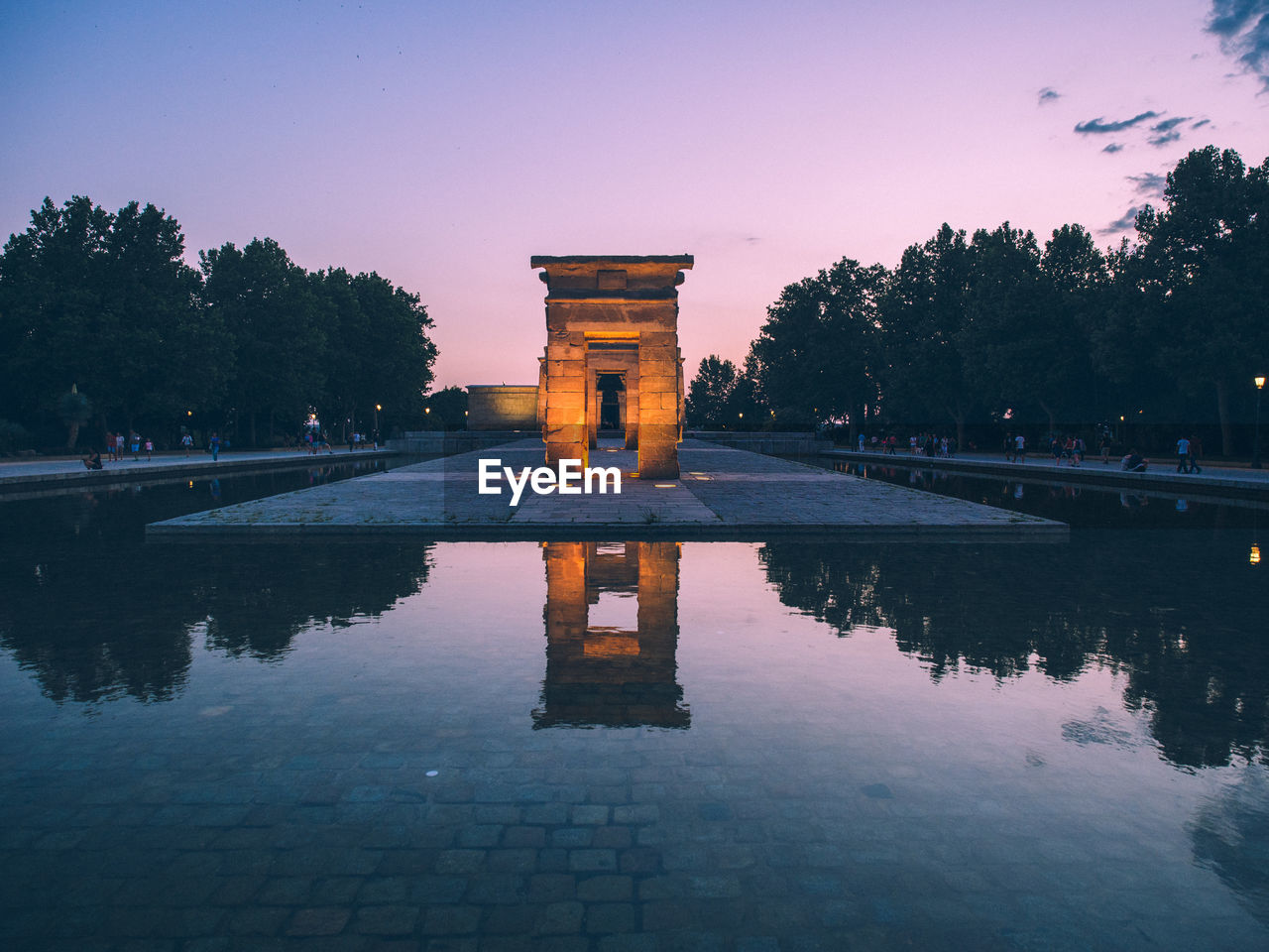 Reflection of built structure in water against sky at sunset