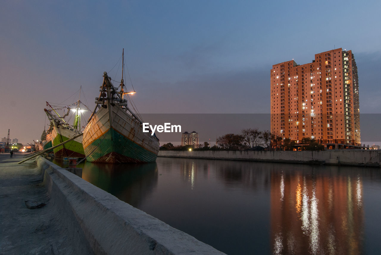 ILLUMINATED BUILDINGS BY CANAL AGAINST SKY AT DUSK