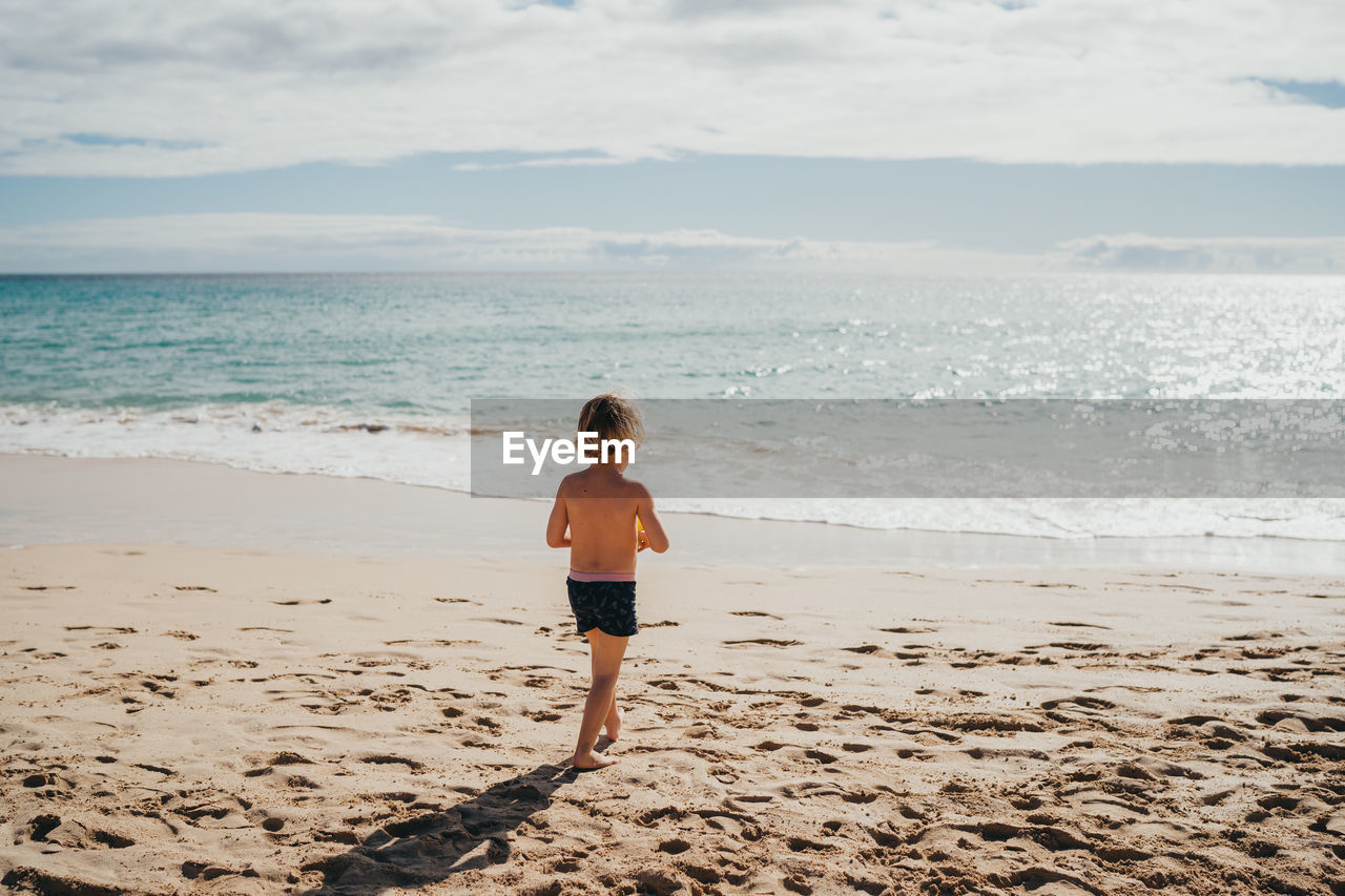 Boy walking into the water at the beach on a sunny day on vacation