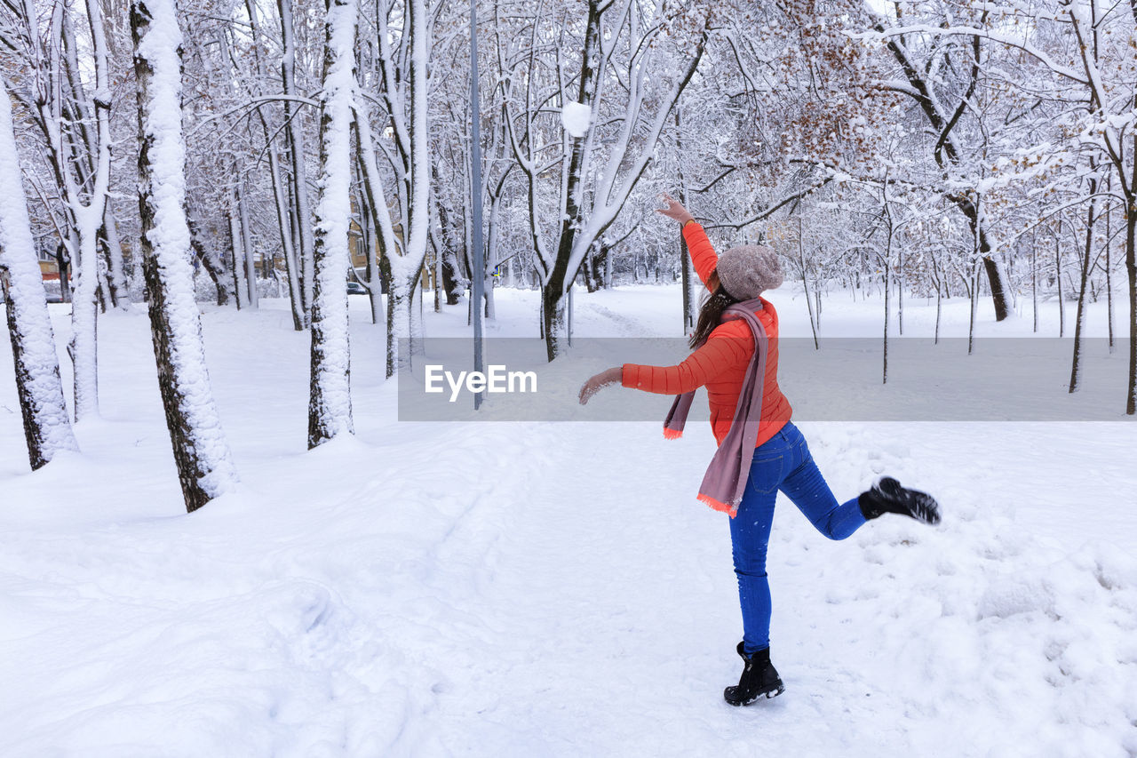 Full length of woman throwing snowball in forest during winter