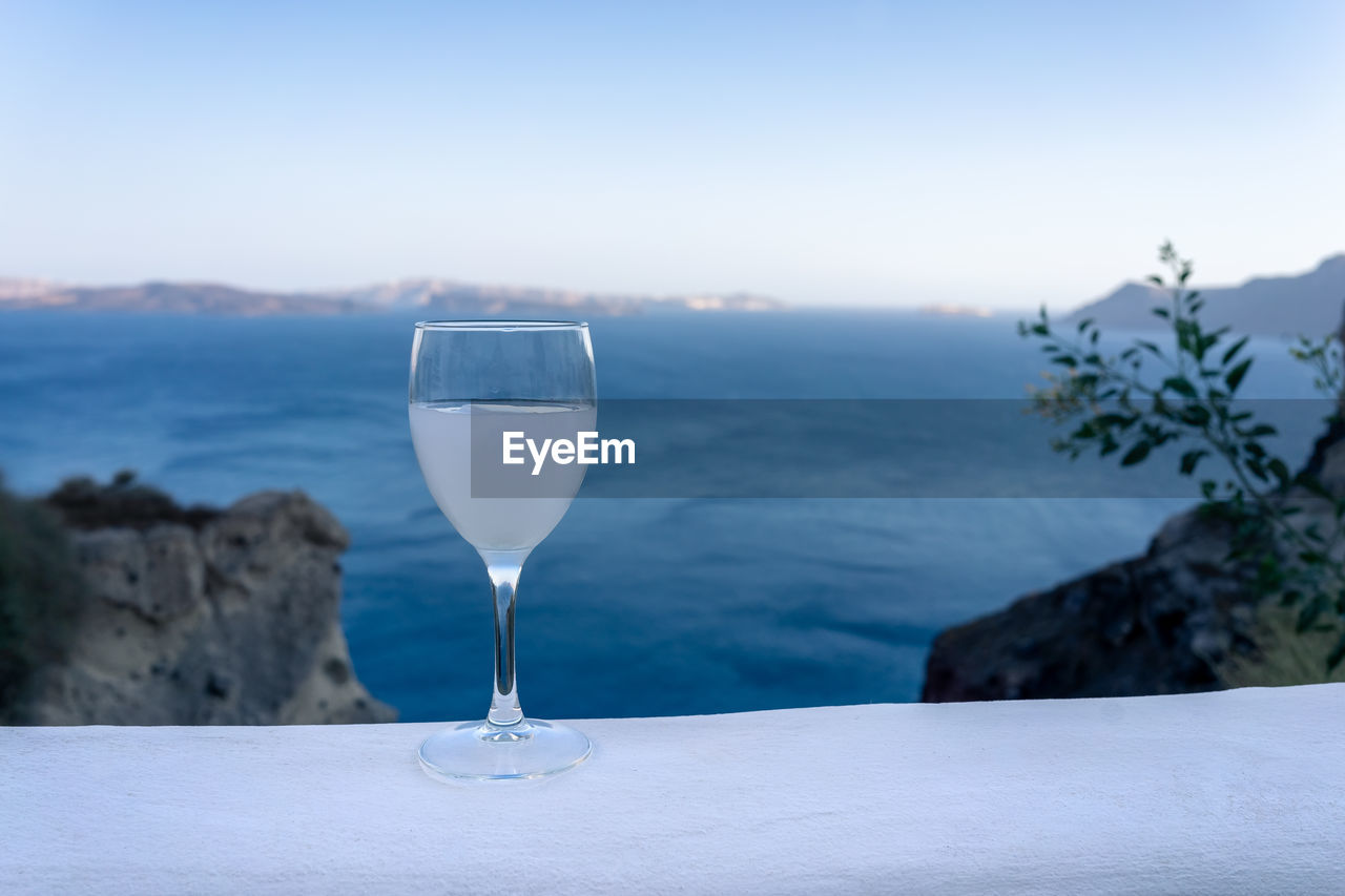 Close up of an ouzo stemmed glass on a white stand during sunset with the santorini caldera