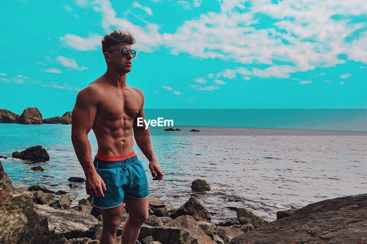 Shirtless man standing on rock at beach