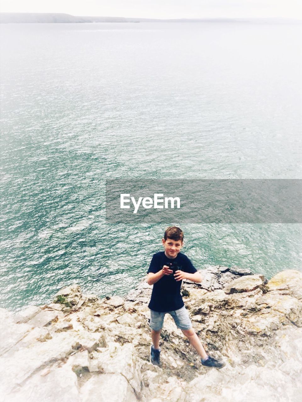 Boy standing on rock by sea