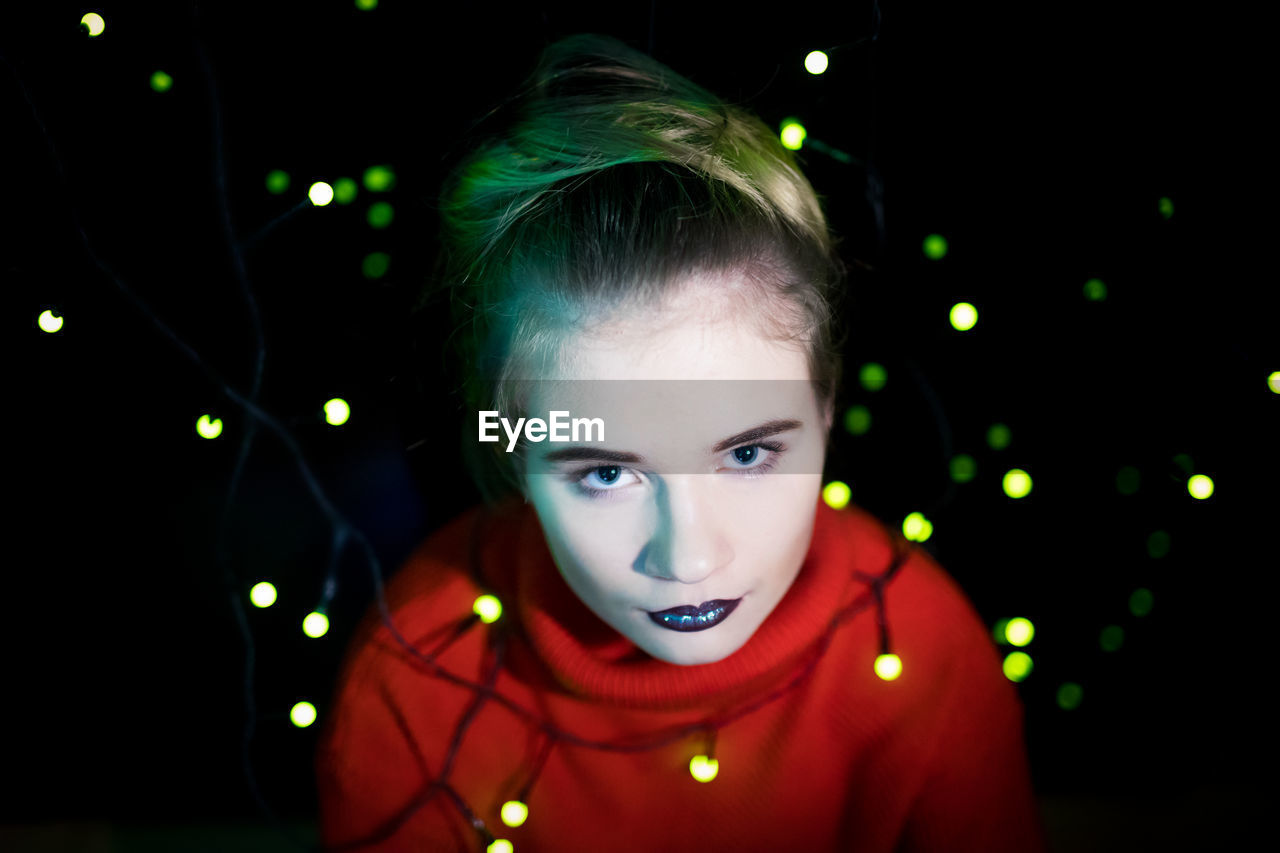 High angle portrait of young woman with illuminated lighting equipment against black background