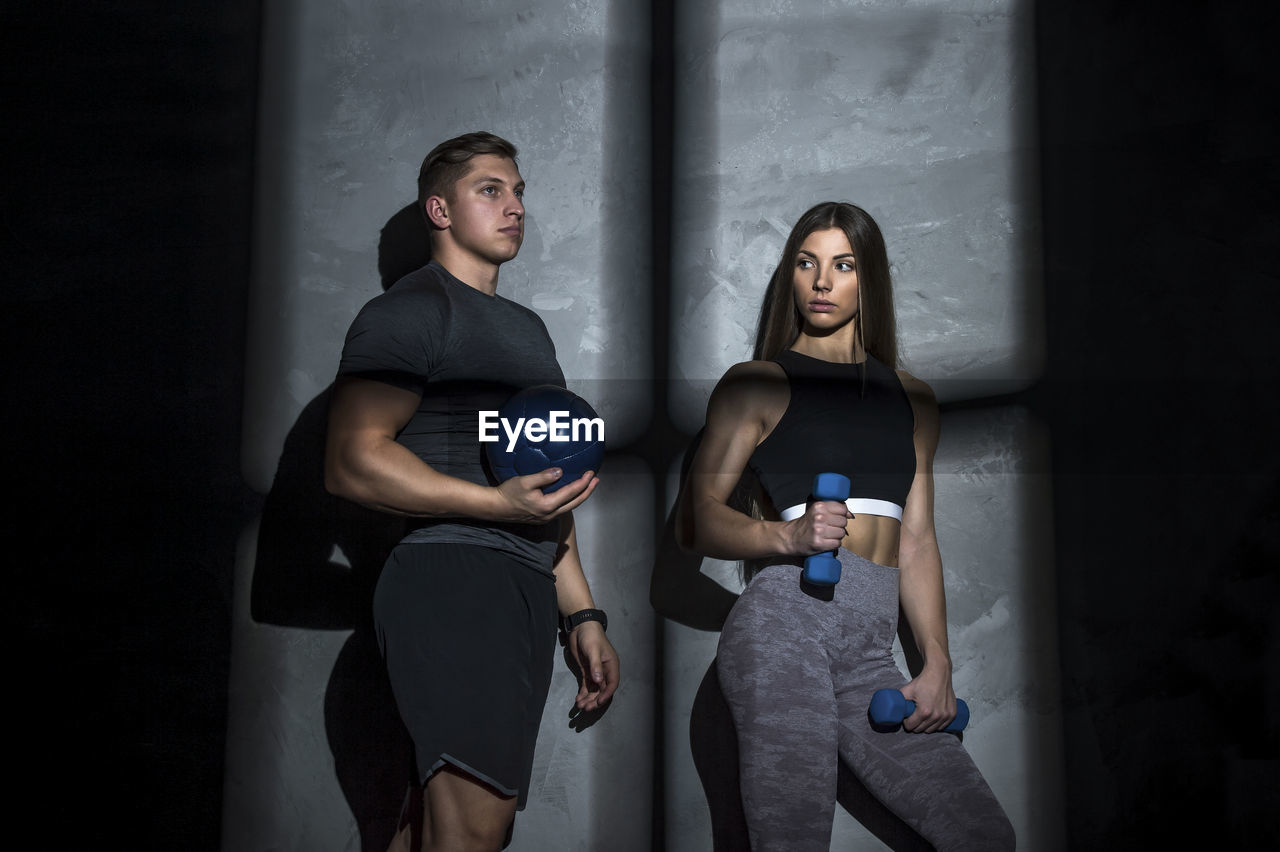 Young couple standing at gym against wall
