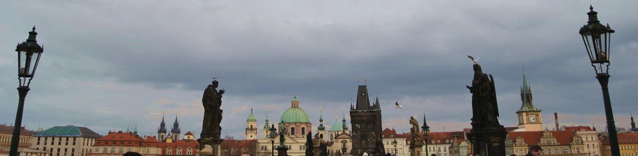 Panoramic view of statues in town square against cloudy sky