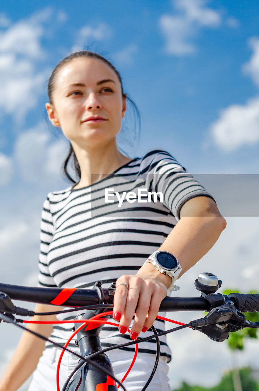 Girl cyclist, portrait against the sky. hand with a smart watch on a bicycle handlebar.