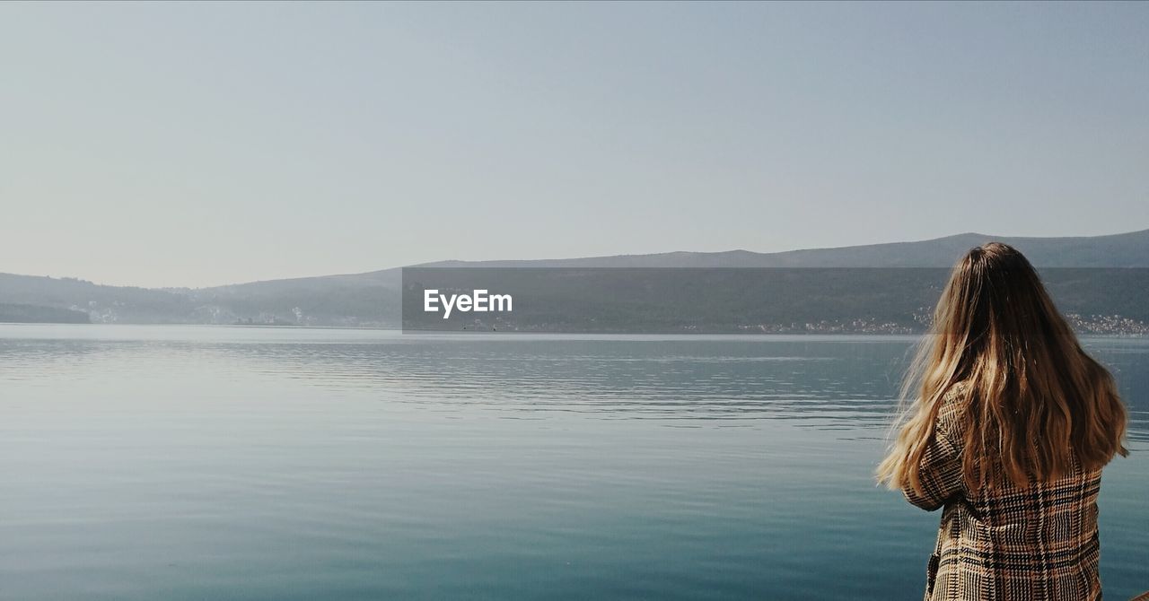 Rear view of woman looking at lake against clear sky