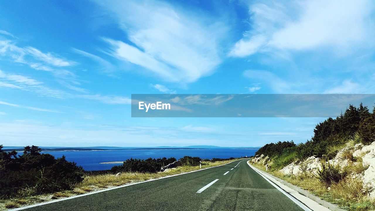 Empty road along trees and against blue sky